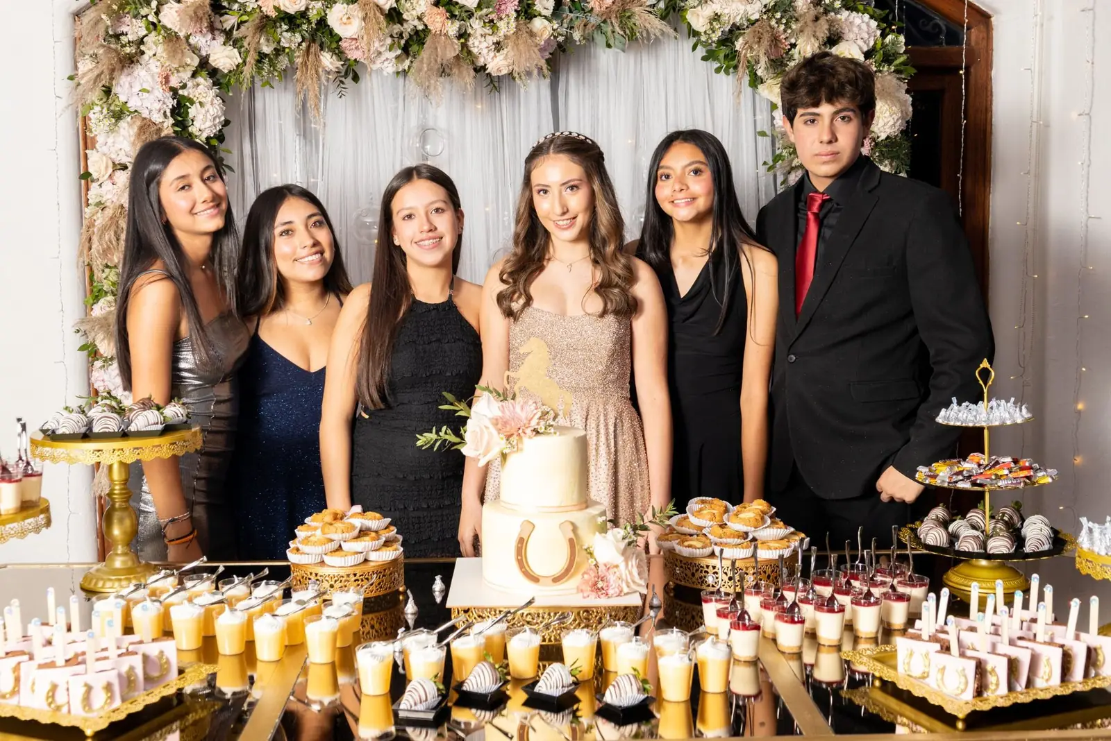 Quinceañera con amigos junto a la mesa de postres y la torta