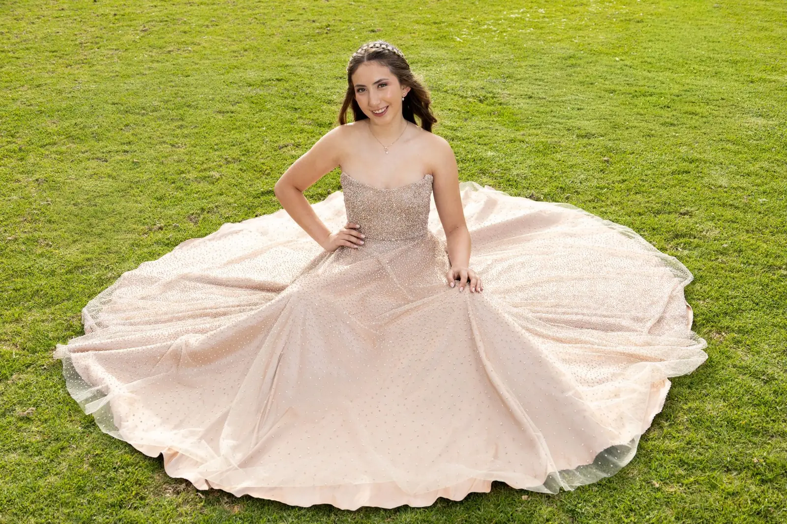 Quinceañera sentada en el pasto con vestido rosado de falda amplia