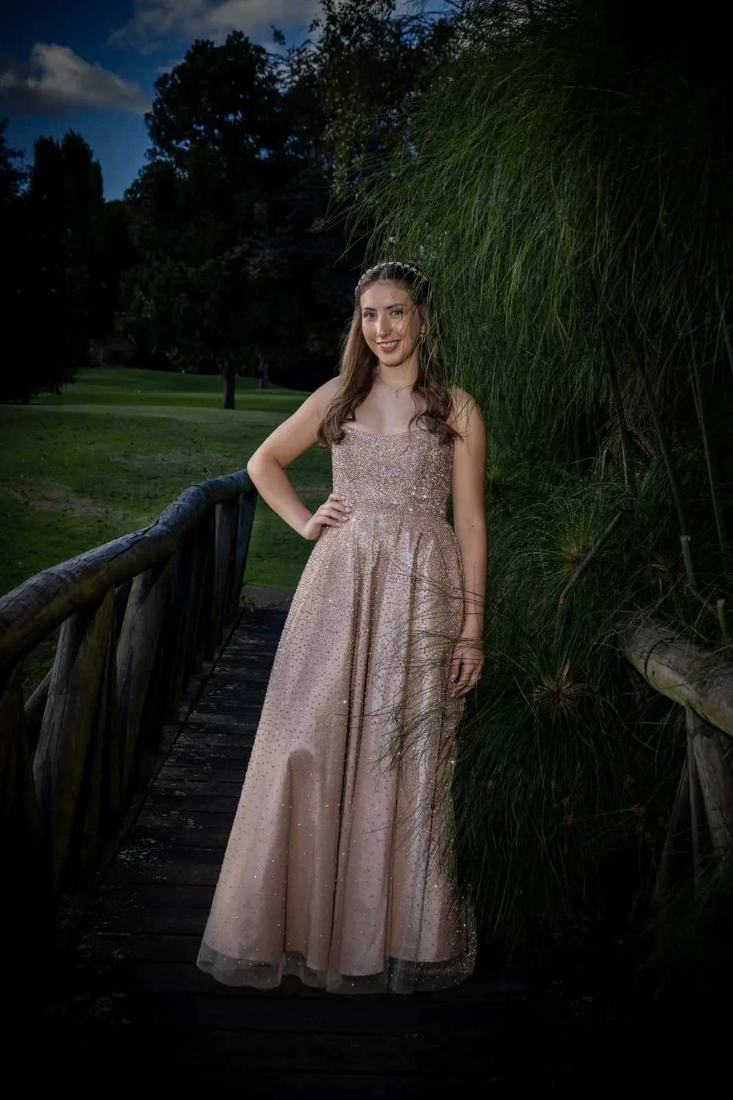 Quinceañera posando junto a pastos altos en un puente al atardecer