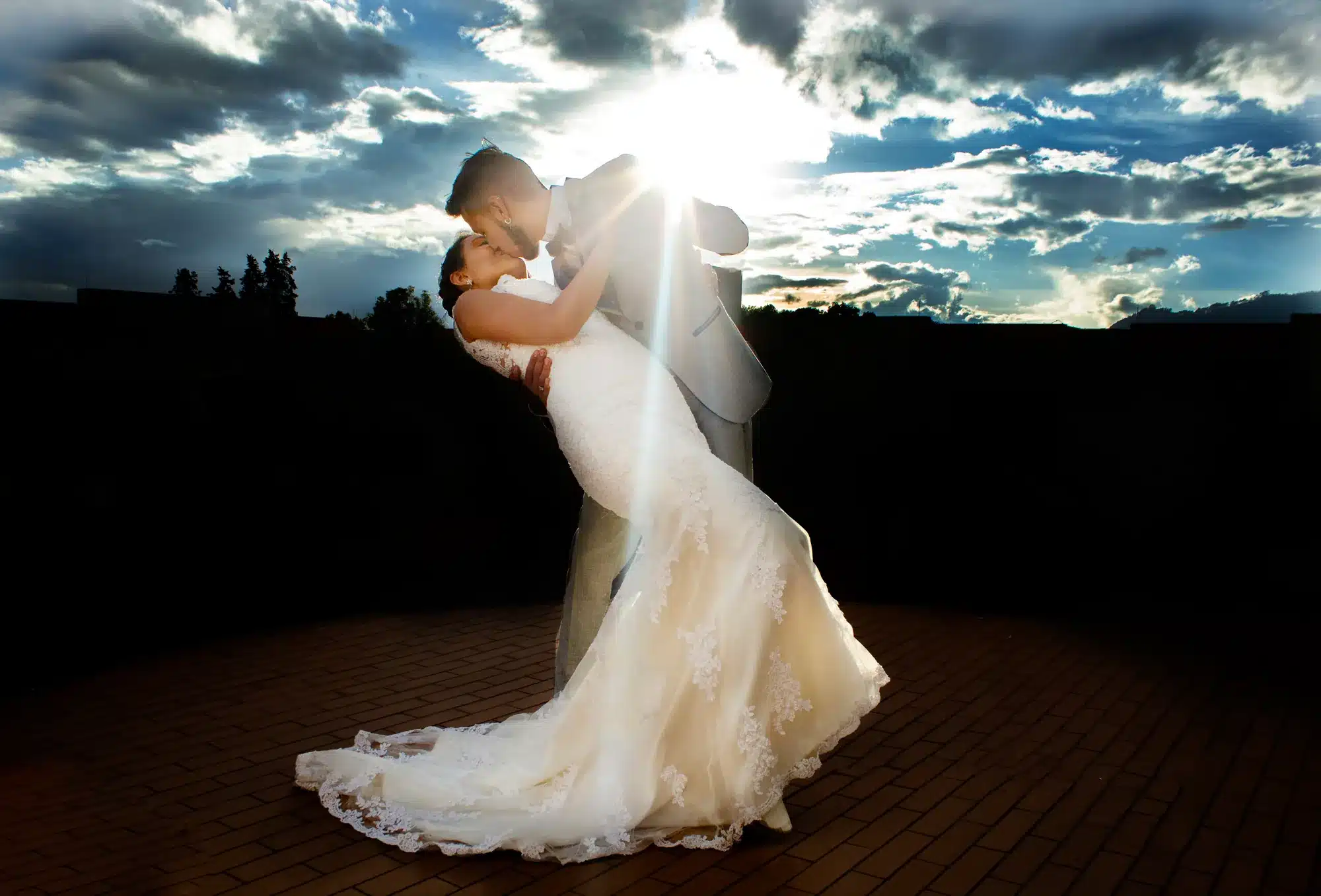 Novios bailando bajo un cielo dramático al atardecer