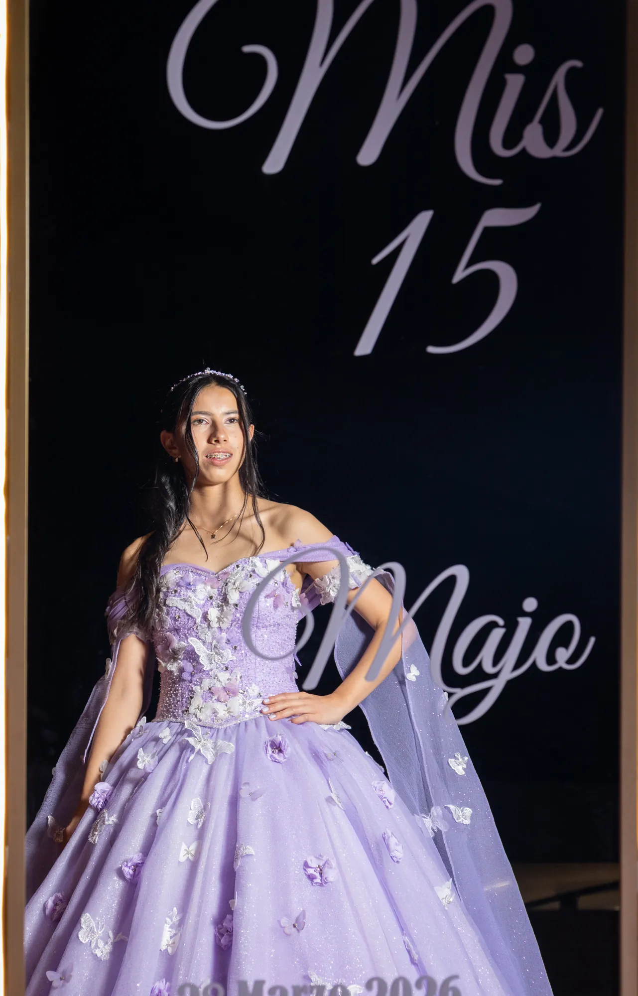 Quinceañera con vestido lila frente a un panel de Mis 15
