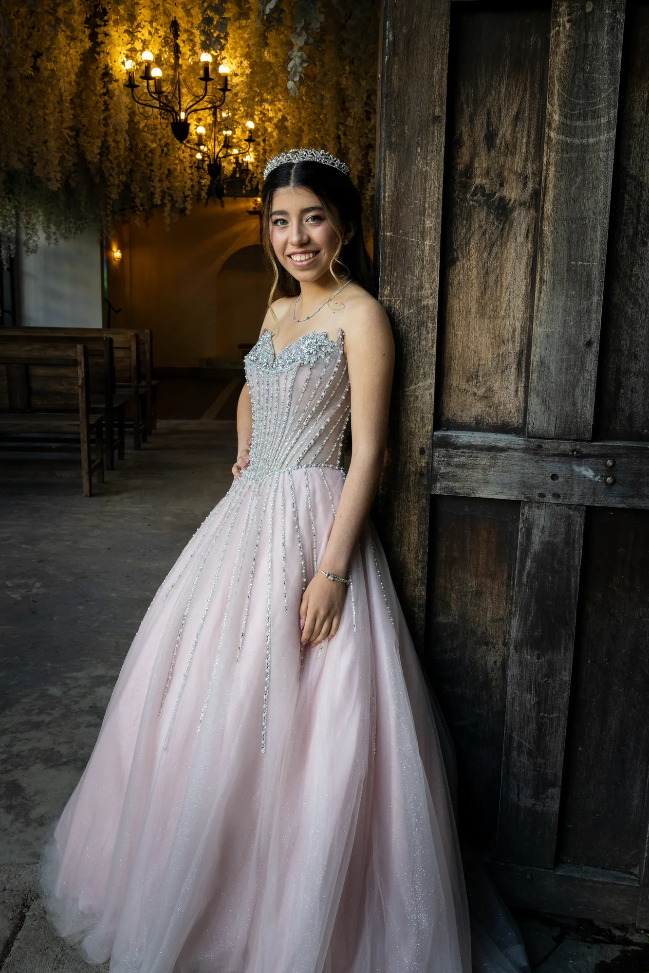 Quinceañera con vestido rosado junto a una puerta de madera