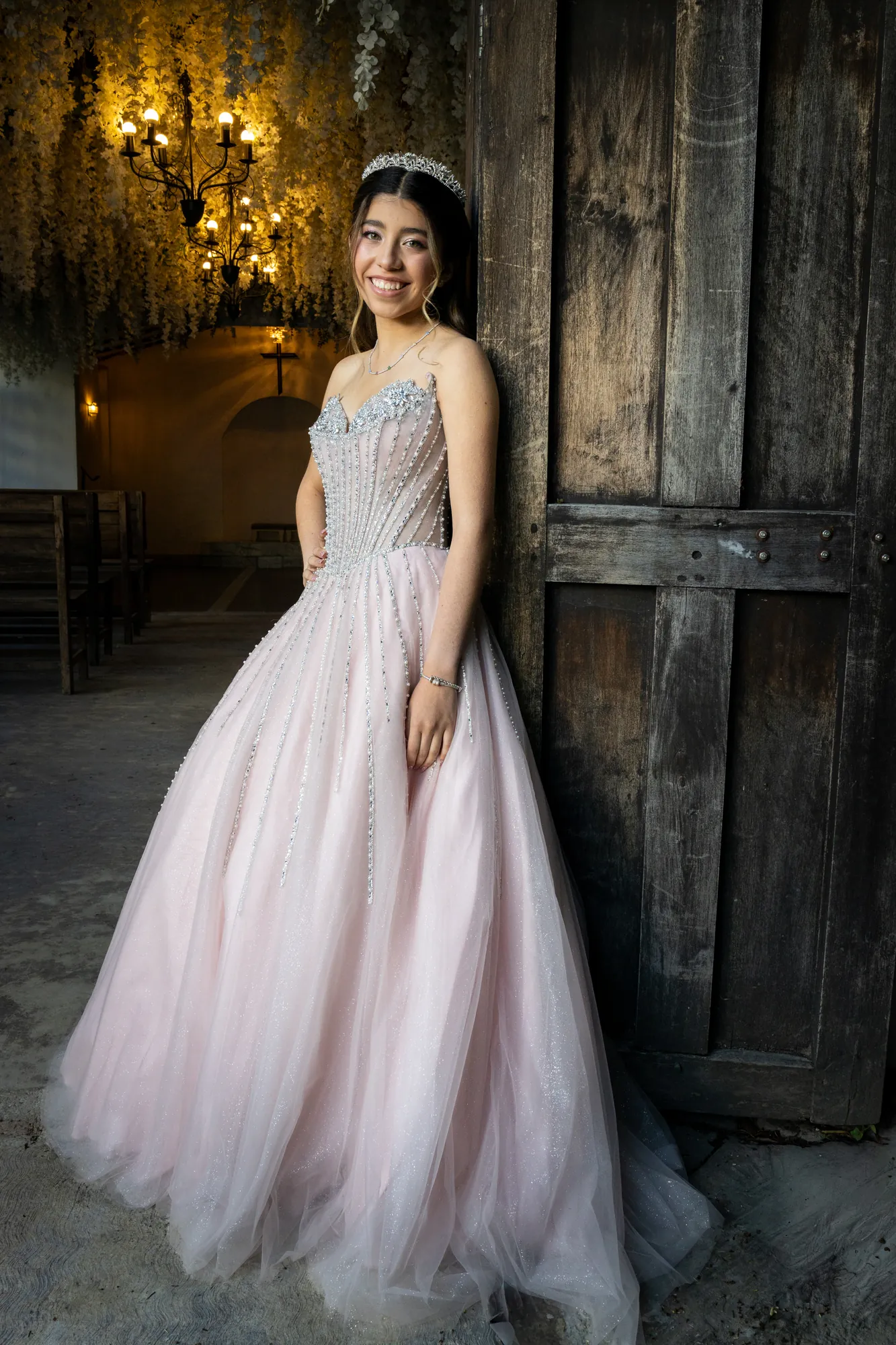 Quinceañera con vestido rosado y corona en un salón rústico