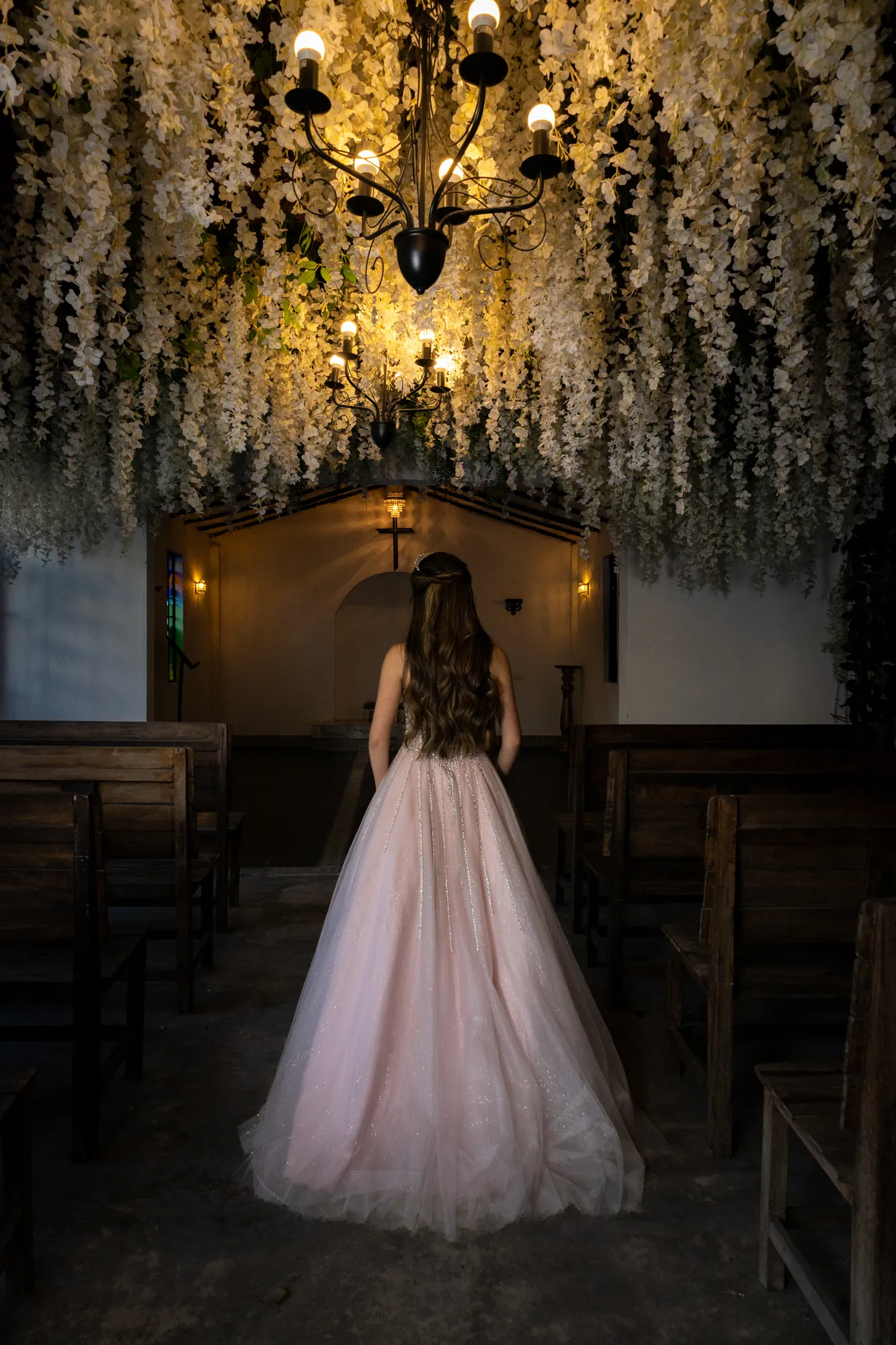 Quinceañera de espaldas con vestido rosado en una capilla