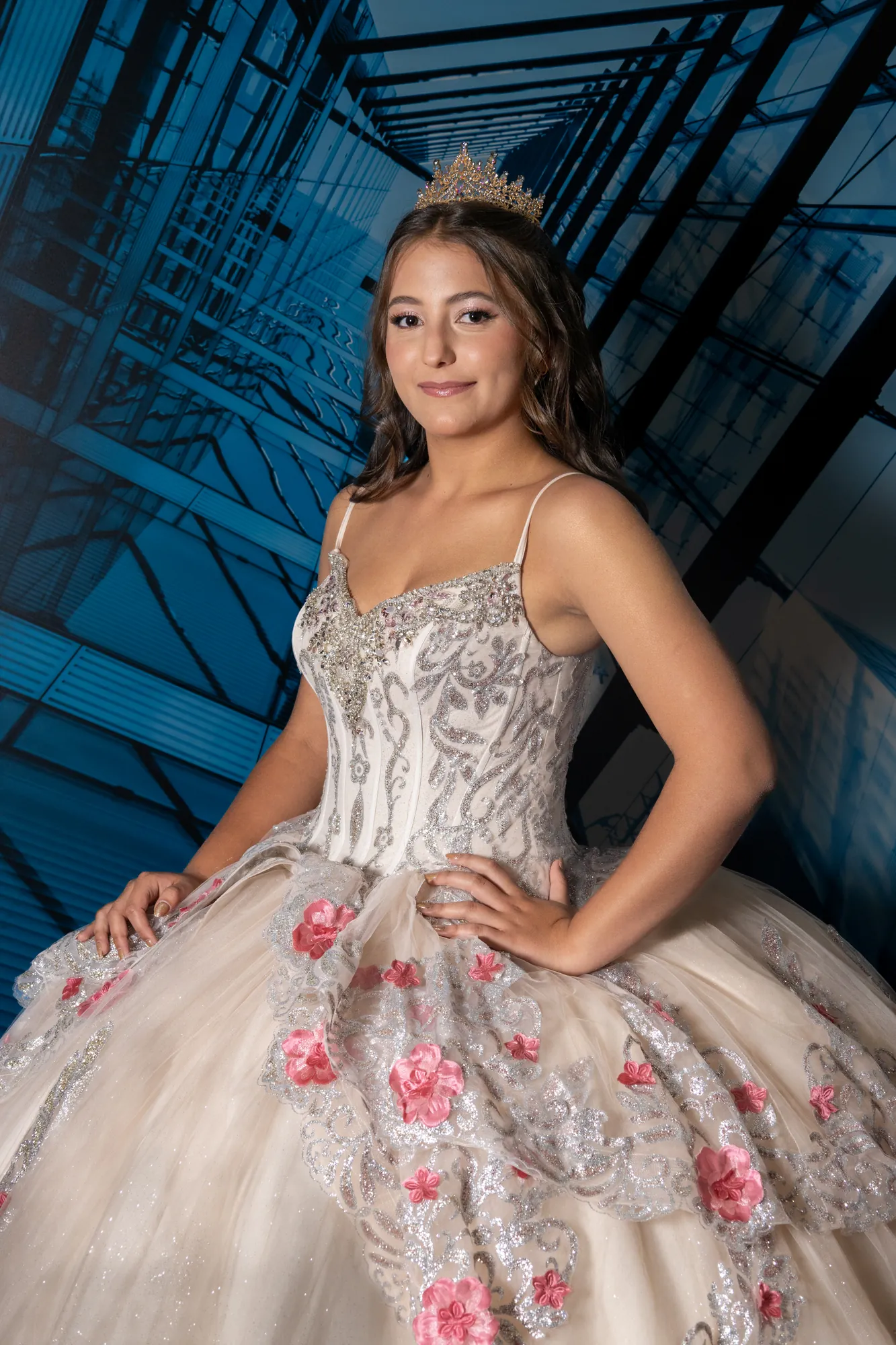 Quinceañera posando frente a un muro de vidrio azul
